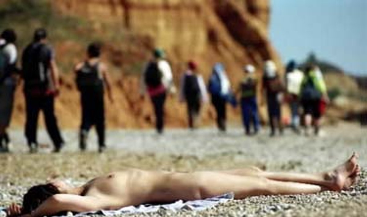 Žmonės nekreipdami dėmesio žingsniuoja pro Sevastopolio paplūdimyje, prie Juodosios jūros  besikaitinančią saulėje nuogą moterį.