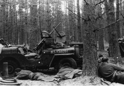 SAS, apšaudomi Vokietijoje: vyrai kairėje slapstosi už džipo, o Paddy Mayne´as, atsirėmęs į medį nugara į kamerą, regis, skaito knygą.