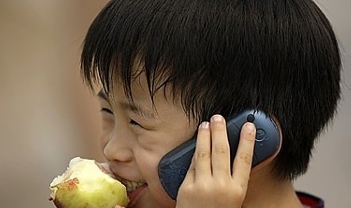 Kinų berniukas valgo obuolį ir kalba mobiliuoju telefonu. Re