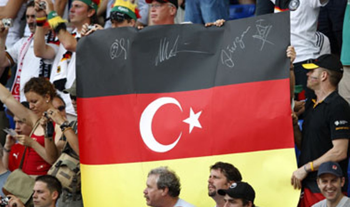 Futbolo gerbėjai laiko Vokietijos vėliavos spalvų plakatą su Mėnuliu ir žvaigžde, kurie puošia Turkijos vėliavą.