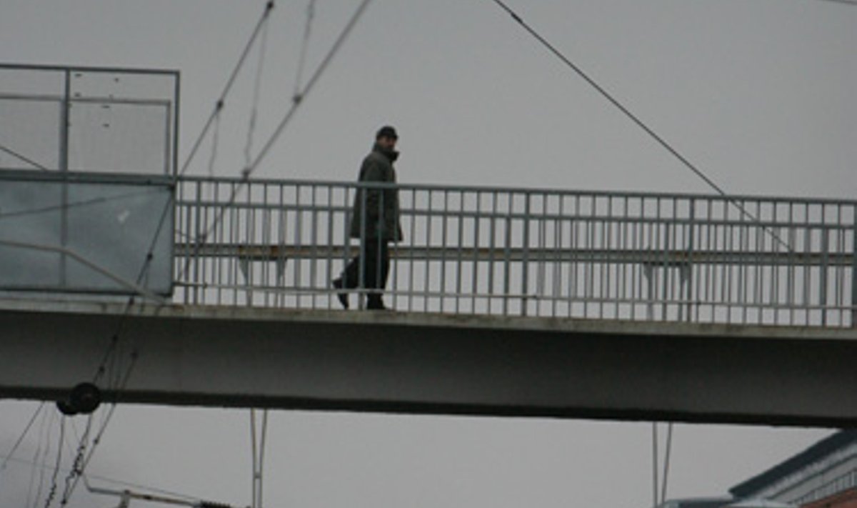 Žmogus eina pėsčiųjų tiltu virš geležinkelio