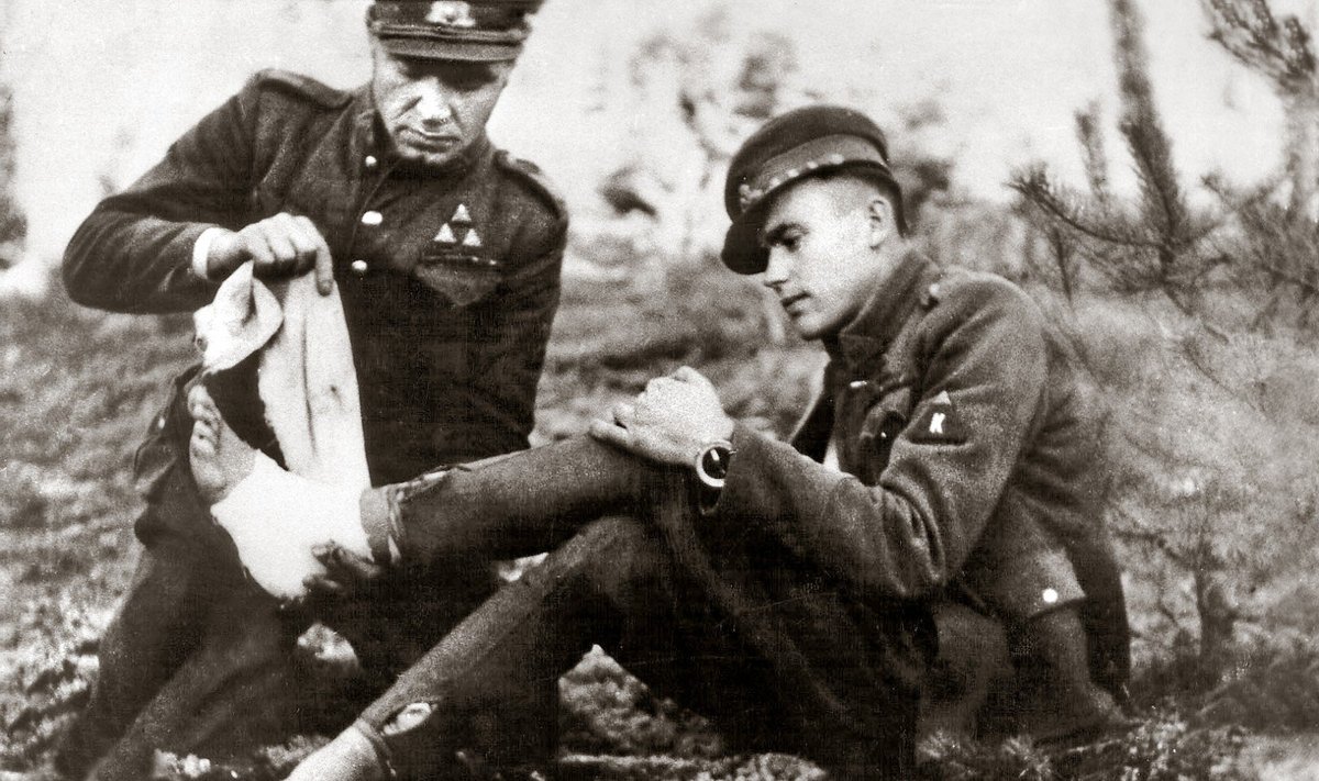 Dainavos apygardos partizanas Feliksas Daugirdas-Šarūnas bintuoja koją bendražygiui Vincui Kalantai-Nemunui. Apie 1949 m. 