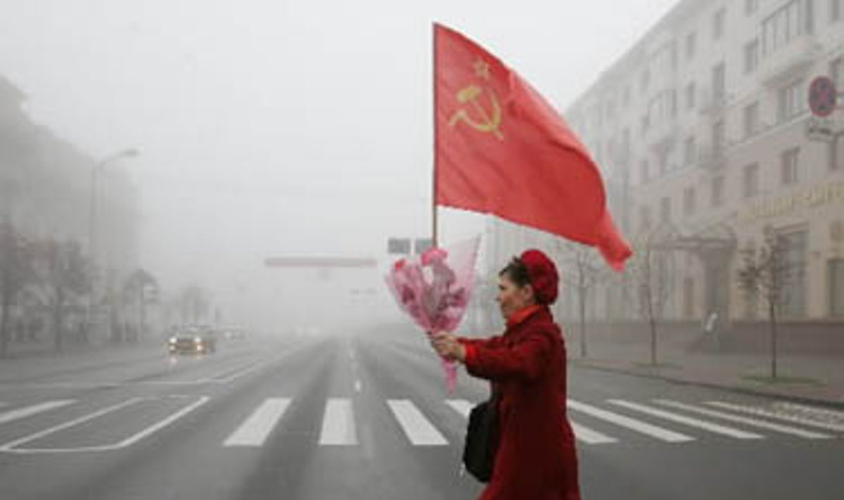 Moteris, nešina gėlėmis ir sovietų vėliava, eina Minsko gatve.