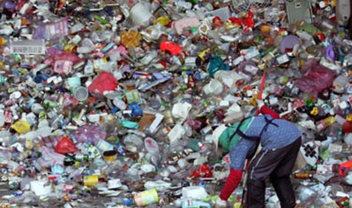 Žmogus stovi prie didelės plastikinių butelių krūvos. Šiame atliekų lauže panaudoti plastikiniai buteliai rūšiuojami ir perdirbami. Taipėjus.