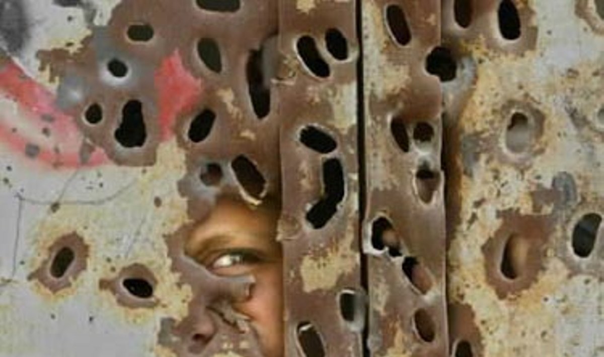 Palestiniečių berniukas žiūri pro kulkų suvarpytas savo namų duris.
