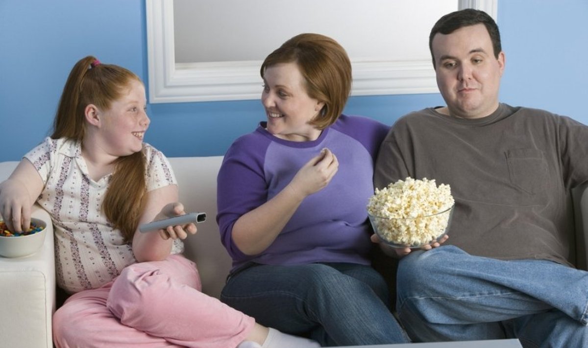 Šeima užkandžiauja žiūrėdami televizorių 