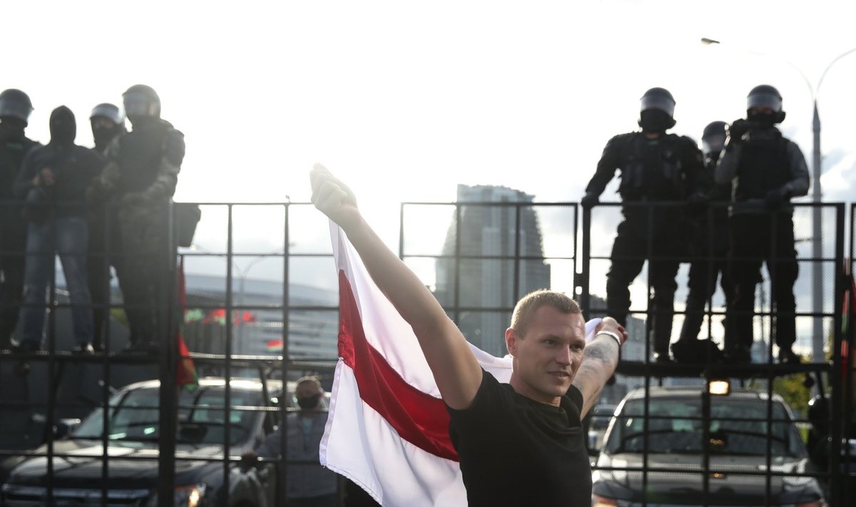 Opozicijos rėmėjas mitingo metu prieš teisėsaugos pareigūnus, blokuojančius gatvę, laiko buvusią Baltarusijos vėliavą
