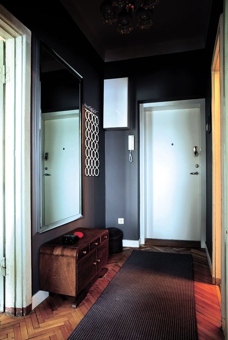 Nedidukas koridorius nudažytas tamsia žemės spalva, kurioje gražiai išryškėja balti durų stačiakampiai ir jų formą atkartojantis veidrodis.