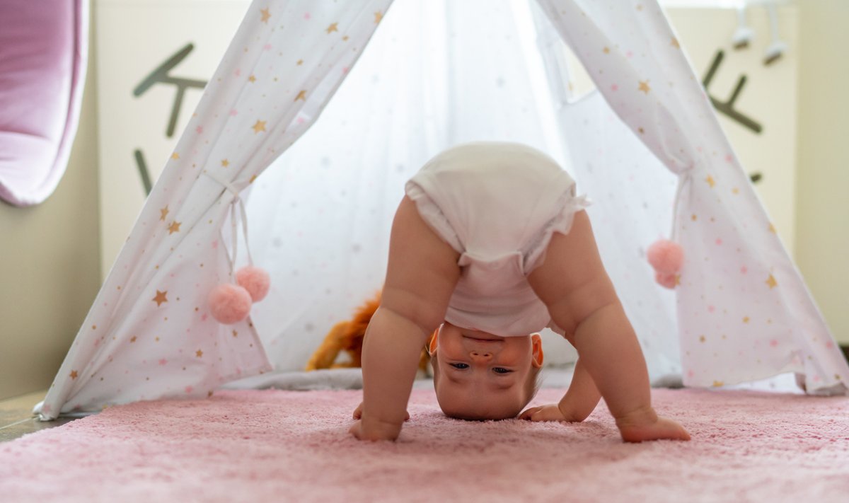 Cute baby girl standing upside down on the carpet in the bedroom