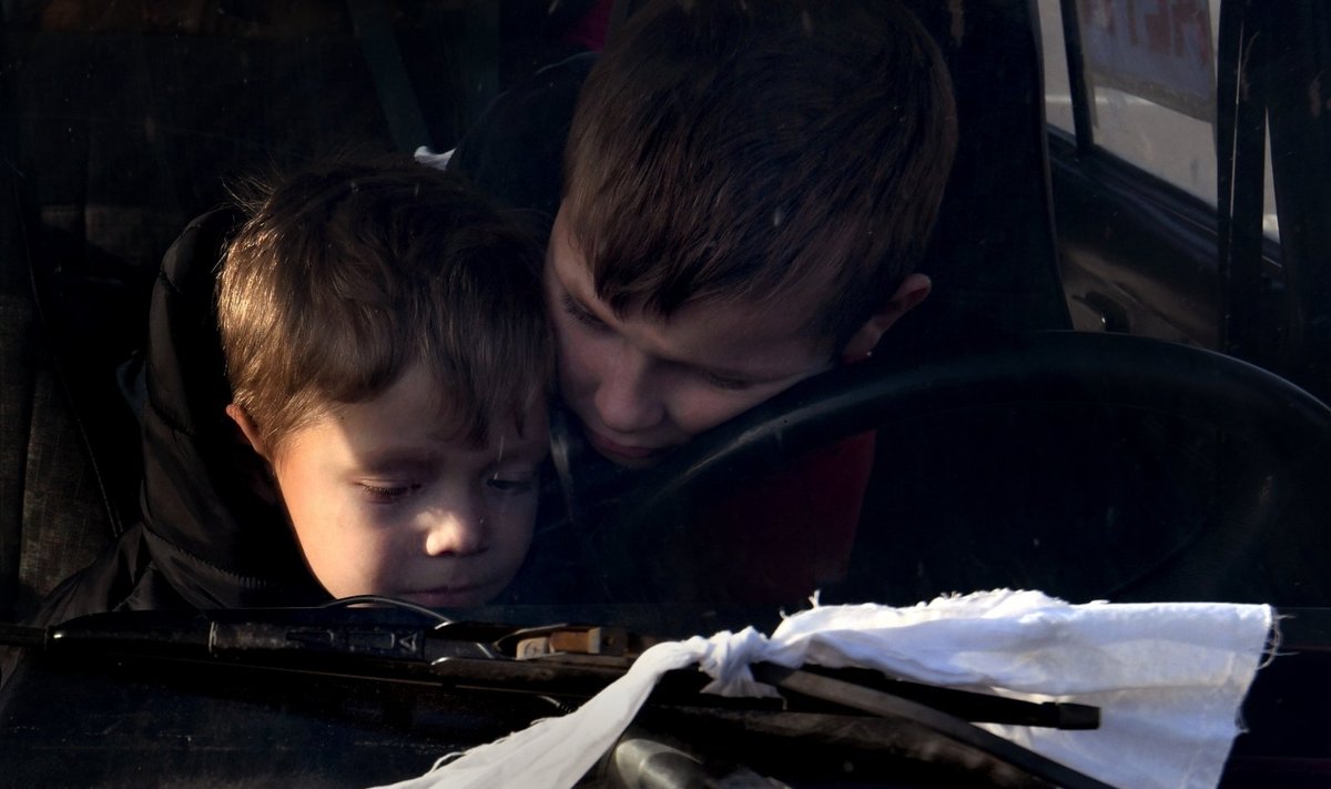 Iš Sartanos, Donetsko regiono kilę Artūras ir Natalija  bei jų vaikai Saša, Vova ir Katya laukia tranzitiniame humanitarinės pagalbos sustojime. Nuotrauka daryta Ukrainos gyventojams bėgant į Zaporižią nuo beviltiškai žiaurių gyvenimo sąlygų Rusijos okupuotame Mariupolyje. Pabėgėliai evakuojasi sudaužytais automobiliai, ant kurių užrišti balti raiščiai ir užrašyta „vaikai“. 2022 kovo 28 d., Ukraina. 