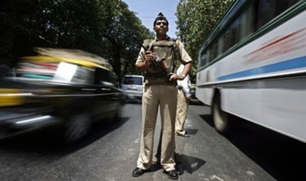 Indijos policininkas stovi tarp važiuojančių mašinų.