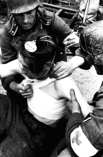 Vermachto medicinos tarnybos sanitarai, nešioję specialius raiščius ant rankovių, tvarsto sužeistąjį