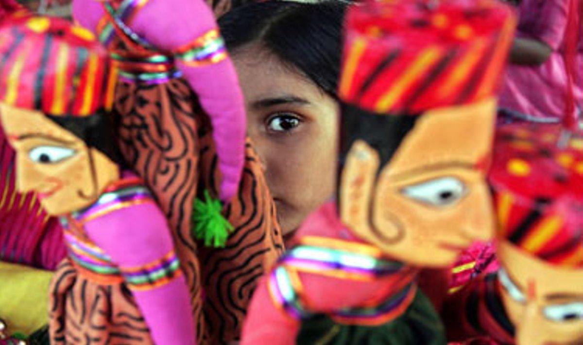Indė mergaitė stebi praeivius šalia Kalkutos amatininkų turgavietėje sukabintų lėlių. 
