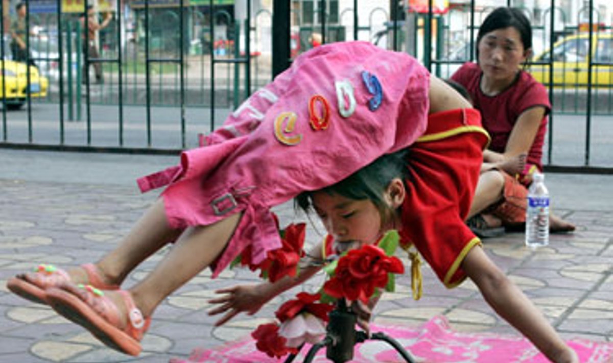 Kinė mergaitė gatvėje 6alia savo motinos atlieka akrobatinius triukus, taip uždirbdama pinigus. 