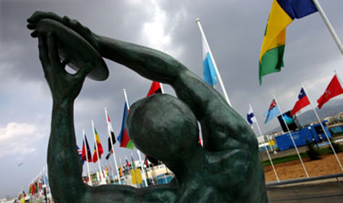 Bronzinė disko metiko skulptūra Atėnuose šalia vėliavų laukia atvykstančių Olimpinių žaidynių dalyvių. 