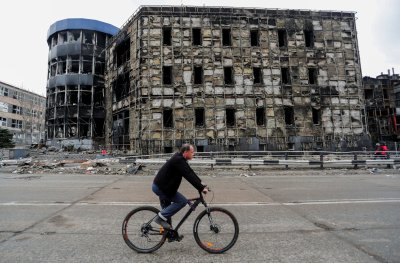 Vyras važiuoja gatve, šalia sunaikinto pastato Mariupolio uostamiestyje, Ukrainoje. 2022 m. balandžio 14 d. Rusijos karas prieš Ukrainą. 