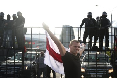 Opozicijos rėmėjas mitingo metu prieš teisėsaugos pareigūnus, blokuojančius gatvę, laiko buvusią Baltarusijos vėliavą