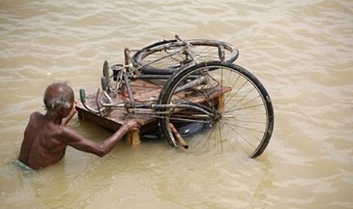 Rytų Indiją niokojant potvyniams, vyras ant lentų plukdo savo dviratį. 