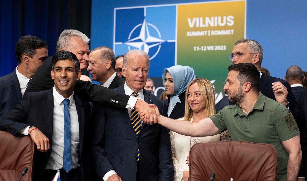 Ukrainian President Volodymyr Zelensky reaches past US President Joe Biden to shake hands with Lithuania's President Gitanas Nauseda ahead a meeting of the NATO-Ukraine Council during the NATO Summit in Vilnius on July 12, 2023. (Photo by Doug Mills / POOL / AFP)