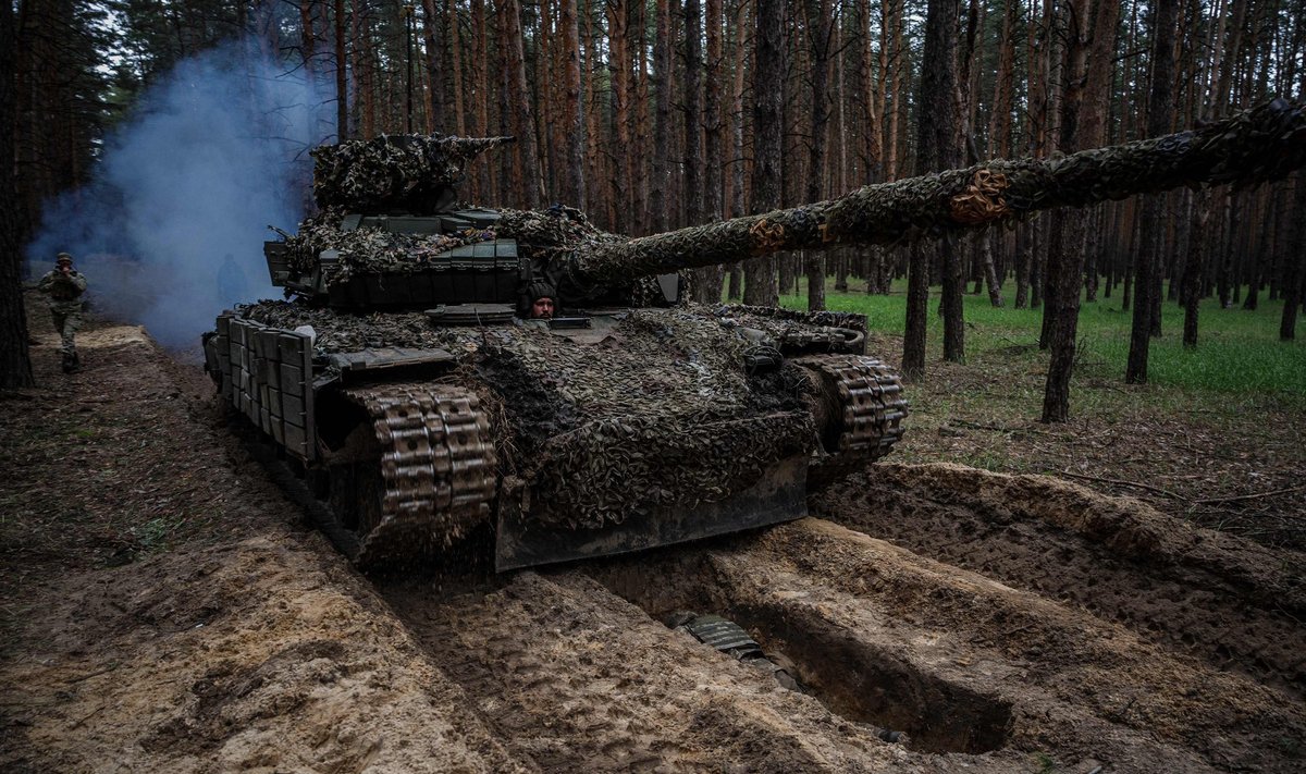 A Ukrainian serviceman lies in a trench while a tank drives over during a military exercise in the Kharkiv region on May 1, 2023, amid the Russian invasion of Ukraine. (Photo by Dimitar DILKOFF / AFP)