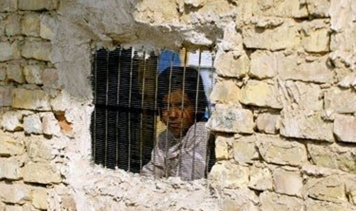 Irakietė žvelgia per grotomis uždengtą langą.