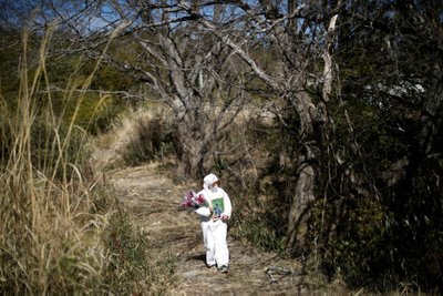 Fukušimos buvusi gyventoja, apsirengusi apsauginį kostiumą, eina aplankyti šeimos kapavietės, kuri nutolusi per 2 kilometrus nuo Fukušimos atominės elektrinės